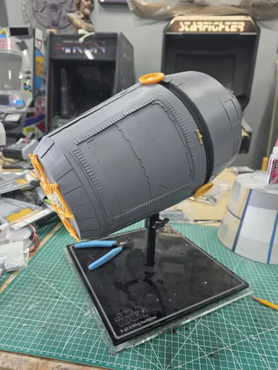 Escape pod model in progress on a black display stand, side view showing raised panel detail and an unpainted orange kit part on the rear