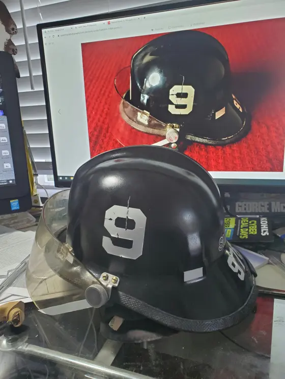 The finished black helmet with a white number 9, clear visor and matched wear marks, in front of a monitor showing a photo of the original stolen helmet for comparison