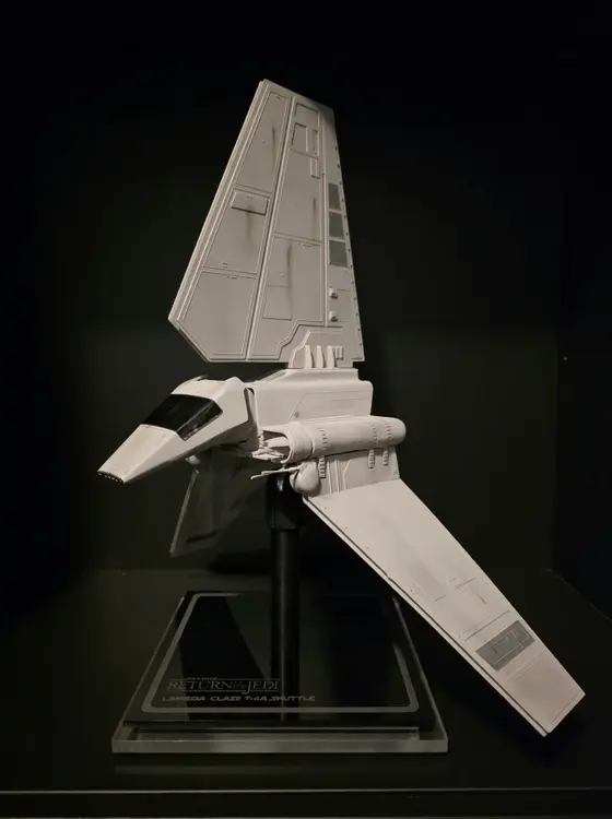 Weathered white Lambda-class shuttle model on a black pole stand, three-quarter view from the nose, above a black acrylic base printed "Return of the Jedi, Lambda Class T-4A Shuttle"