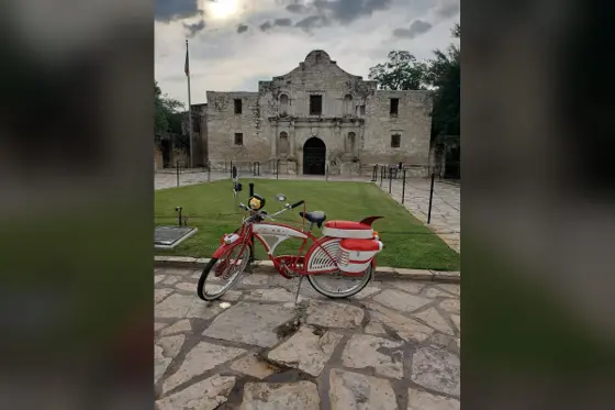 Red and white replica of Pee-wee Herman's bike parked in front of the Alamo